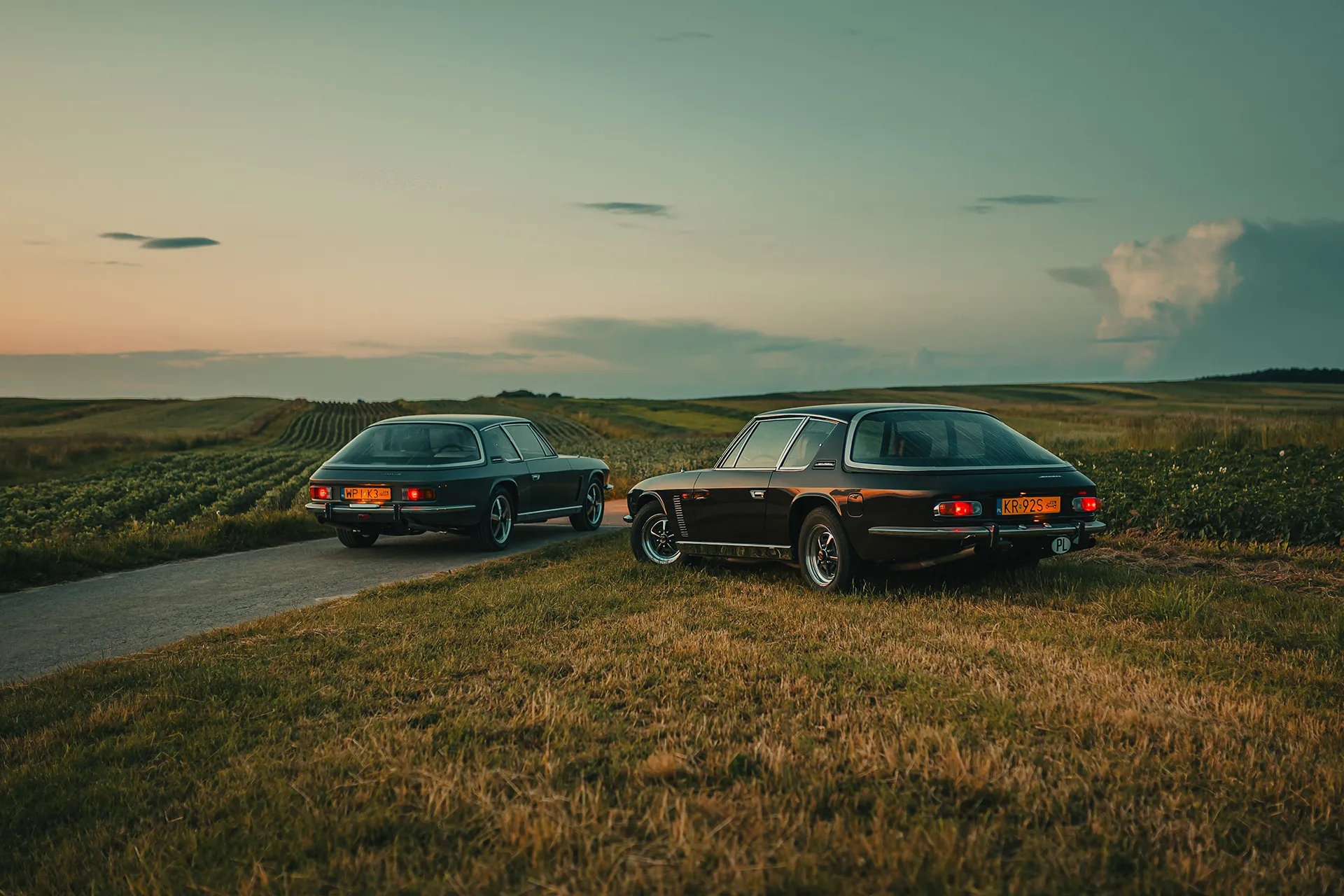 Jensen Interceptor Mk III i Mk II od tyłu na polach w Sułoszowej o zmierzchu